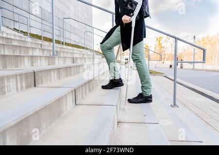 Injured man trying to walk on crutches up the stairs. Stock Photo