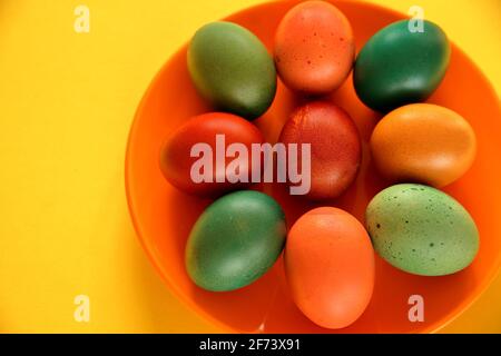 Colorful painted easter eggs on orange plate close up yellow background. Stock Photo