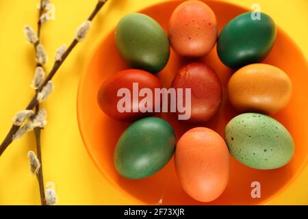 Colorful traditionally painted Easter eggs on orange plate decorated with fresh spring twigs of plants close up yellow background Stock Photo
