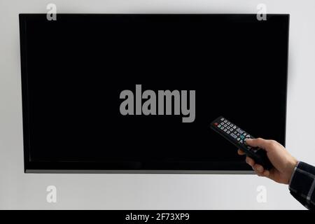 Hand Pointing Remote Control At Empty TV Screen At Home Stock Photo