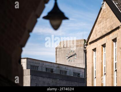 Concrete Art Deco clock tower with Roman numerals on top of retro department store in town centre viewed from under bridge archway with 1950's old out Stock Photo