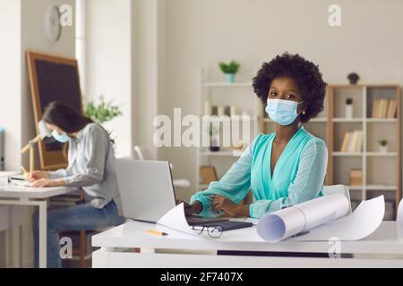 Architect or designer in face mask working on laptop sitting at table in studio office Stock Photo