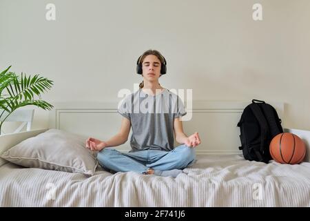 Male teenager sitting in lotus position on bed relaxing meditating Stock Photo