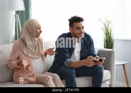 Pregnant muslim lady offended to her careless husband playing video games Stock Photo