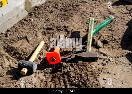 Defocus hammer, mallet, chisel and bayonet of the shovel lie on the ground. Set of tools for laying paving stones. Basic tools to demolish and repair. Stock Photo