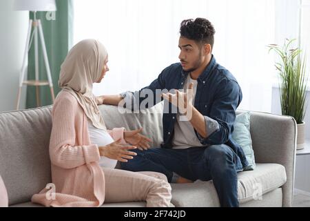 Pregnancy And Relationship Problems. Pregnant Muslim Spouses Arguing At Home Stock Photo