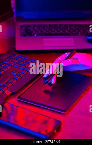 Digital design concept with a robot. Creative designer workplace in neon light. Digital tablet for drawing and an artificial arm with a pen. Distant w Stock Photo