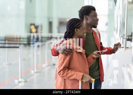 Happy African couple with foreign passports and boarding passes standing at airport check-in counter Stock Photo