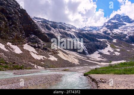 View of snow glaciers with a waterfall and a river in a mountain valley. Toned Stock Photo