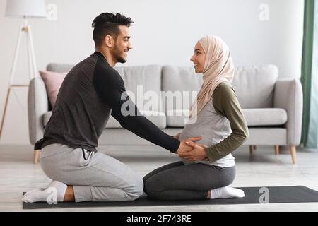 Pregnancy Workout. Happy Muslim Spouses Practicing Yoga Together At Home, Side View Stock Photo