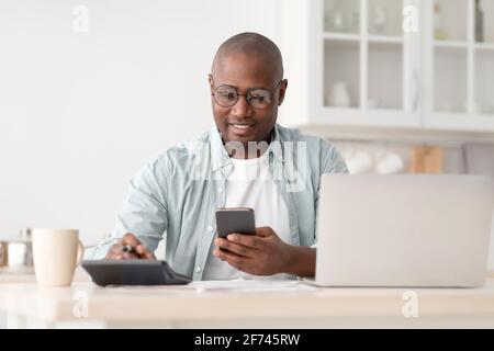 Savings and finances concept. Mature black man using calculator, phone and laptop computer Stock Photo