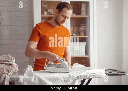 Young man ironing children's sheet on ironing board at home Stock Photo