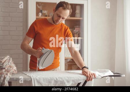 Young man ironing children's sheet on ironing board at home Stock Photo