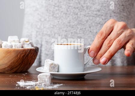 A caucasian Turkish woman is drinking traditional Turkish coffee from special cup. The coffee is served with Turkish delight  on the side of the plate Stock Photo