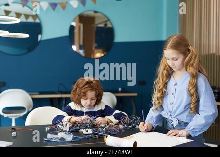 Portrait of boy and girl drawing schemes while building robots during engineering class at school, copy space Stock Photo