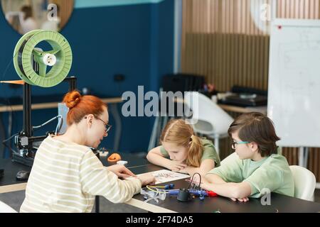 Portrait of two cute children listening to female teacher during engineering and robotics class at modern school, copy space Stock Photo