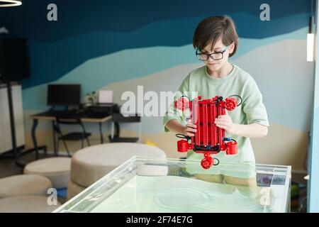 Portrait of boy putting robo boat in water while experimenting with technology at robotics lab in school, copy space Stock Photo