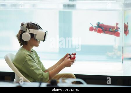 Side view portrait of boy wearing VR headset while operating robotic boat in school laboratory, copy space Stock Photo