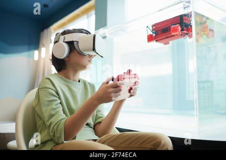 Low angle portrait of boy wearing VR headset while operating robotic boat in school laboratory, copy space Stock Photo