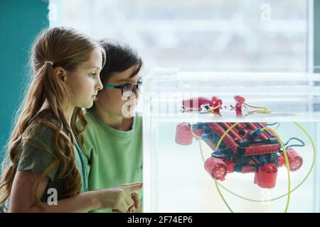 Side view portrait of two children operating robotic boat in water tank while experimenting in engineering lab at school, copy space Stock Photo
