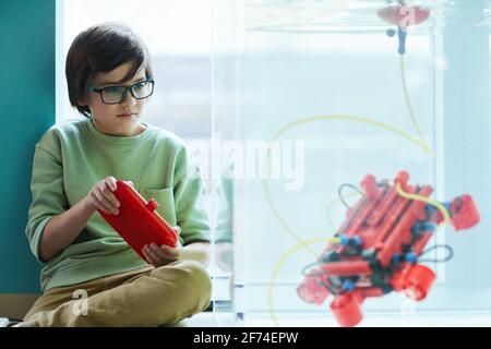 Portrait of smart boy operating robotic boat in water tank while experimenting in engineering lab at school, copy space Stock Photo