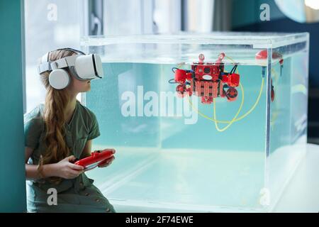 Side view portrait of girl wearing VR headset while operating robotic boat in school laboratory, copy space Stock Photo
