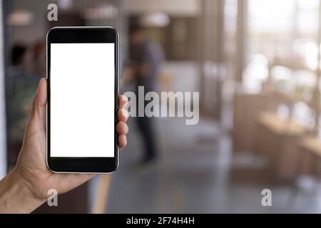 Hand man holding black mobile phone with blank white screen with blur coffee shop background. Mockup image of hand holding smartphone with blank white Stock Photo