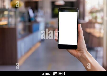 Hand women holding black mobile phone with blank white screen with blur coffee shop background. Mockup image of hand holding smartphone with blank whi Stock Photo