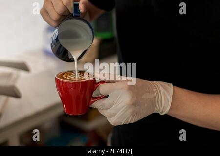 Close up barista pouring steamed milk into coffee cup making beautiful latte, cappuccino art Rosetta pattern. Close up barista hands pouring warm milk Stock Photo