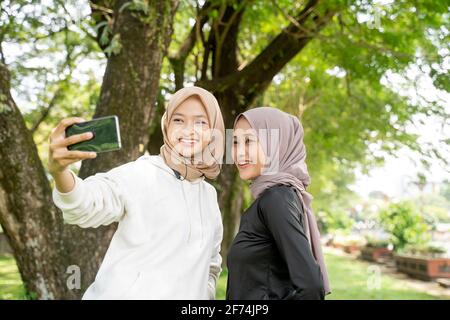 muslim friend taking selfie or video calling outdoor using her smart phone during sport break outdoor Stock Photo