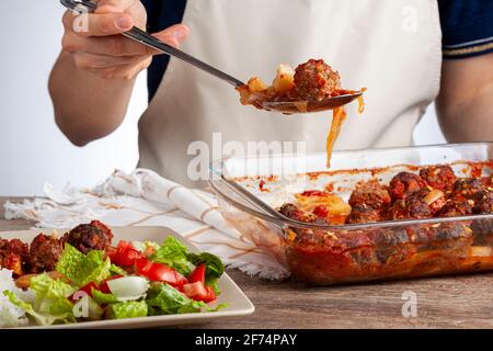 Traditional Turkish recipe, meatballs in tomato sauce, potatoes and onion rings cooked in oven. The meal called kofteli patates is served with salad a Stock Photo