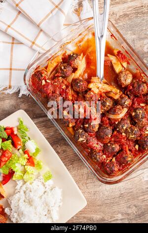 Traditional Turkish recipe, meatballs in tomato sauce, potatoes and onion rings cooked in oven. The meal called kofteli patates is served with salad a Stock Photo