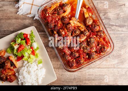 Traditional Turkish recipe, meatballs in tomato sauce, potatoes and onion rings cooked in oven. The meal called kofteli patates is served with salad a Stock Photo