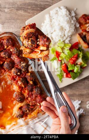 Traditional Turkish recipe, meatballs in tomato sauce, potatoes and onion rings cooked in oven. The meal called kofteli patates is served with salad a Stock Photo