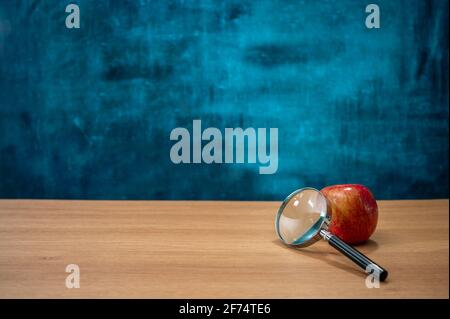 Apples and magnifying glass on the desk. Empty blackboard. Education concept. Stock Photo