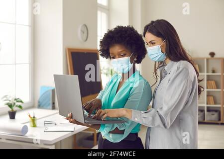 Business women or office workers in medical face masks using laptop computer together Stock Photo