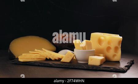 Several types of yellow cheese in chunks and cut into slices on black background. Stock Photo