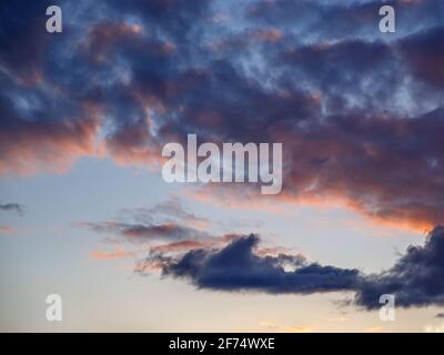 Dark clouds are illuminated by setting sun in spring sky. Stock Photo
