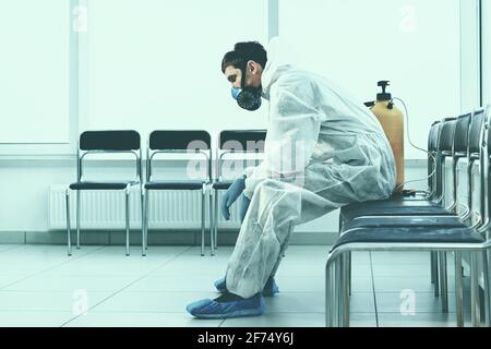 tired medical orderly in a protective suit sitting in a public waiting room. Stock Photo