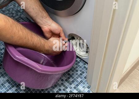 a plumber drains a cart from a broken washing machine through a hose Stock Photo
