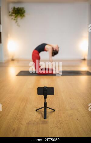 High angle side view of slim female bending back in Ustrasana and shooting live video on smartphone during yoga training Stock Photo