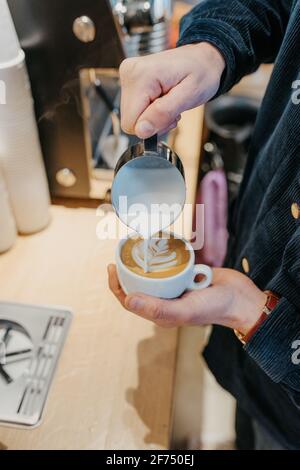From above of crop anonymous barista pouring milk into cup of coffee while making latte art in cafeteria Stock Photo
