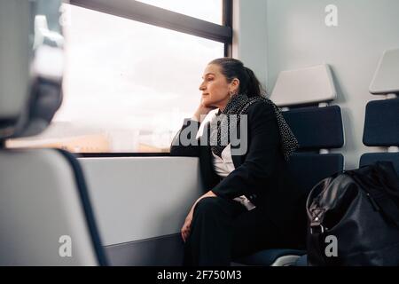 Glad ethnic female student sitting on bench with earbuds in charging case while having break in university campus Stock Photo