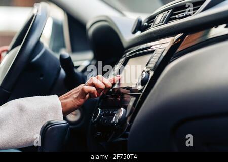 Crop anonymous female touching screen of multimedia control panel in luxury automobile in daytime Stock Photo