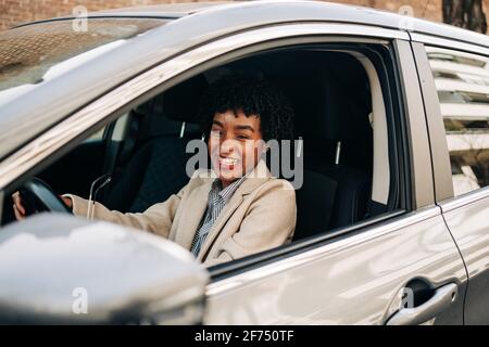 Side view of cheerful African American female driver in fashionable outfit smiling while driving modern automobile on the street Stock Photo