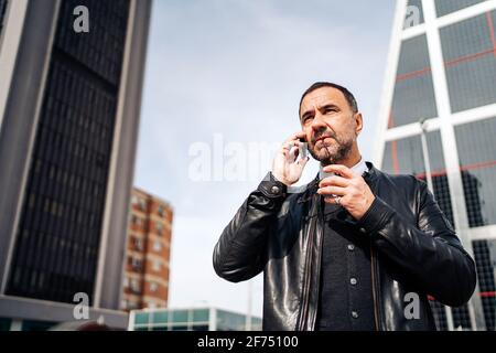 Mature Hispanic male executive in smart casual wear talking on cellphone while walk through the city Stock Photo