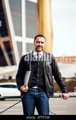 Confident middle aged ethnic male entrepreneur in stylish clothes with netbook looking at camera in city Stock Photo