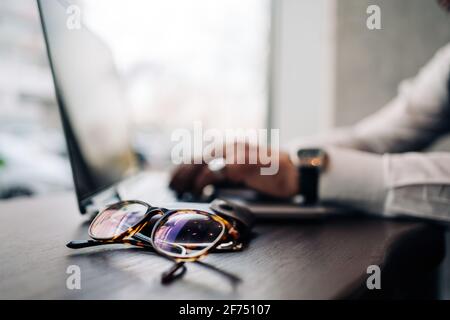 Crop anonymous male executive using portable computer at table with modern eyeglasses in cafe Stock Photo