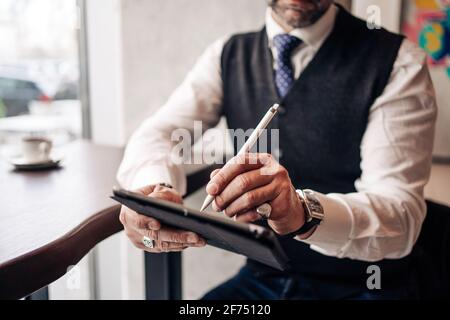 View of crop anonymous male executive using stylus and cellphone at cafeteria table Stock Photo