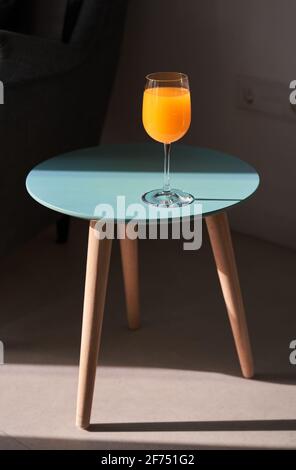 From above of glass of fresh orange juice placed on small round table near comfortable sofa in sunlight